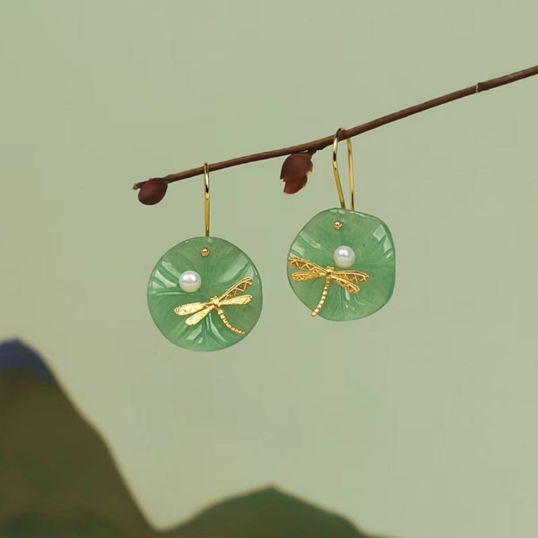Green earrings with gold accents and pearls hanging on a branch against a green background