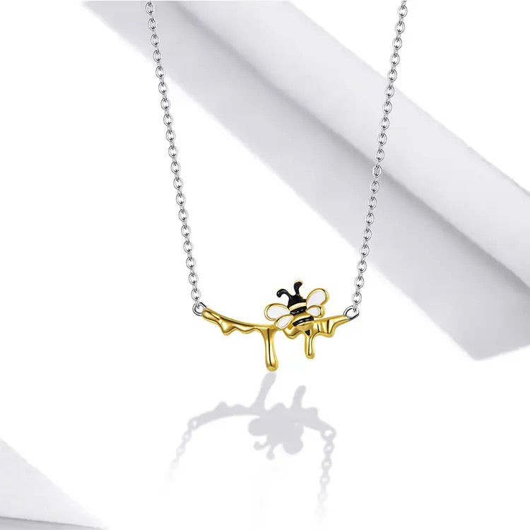 A sterling silver necklace with a gold-plated bee pendant on a white enamel background