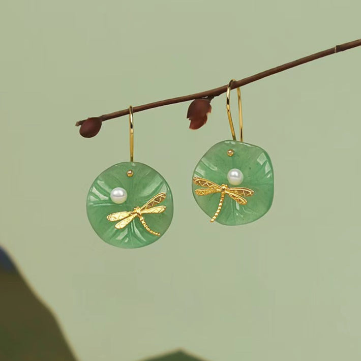 Green earrings with gold accents and pearl centers on a branch against a green background