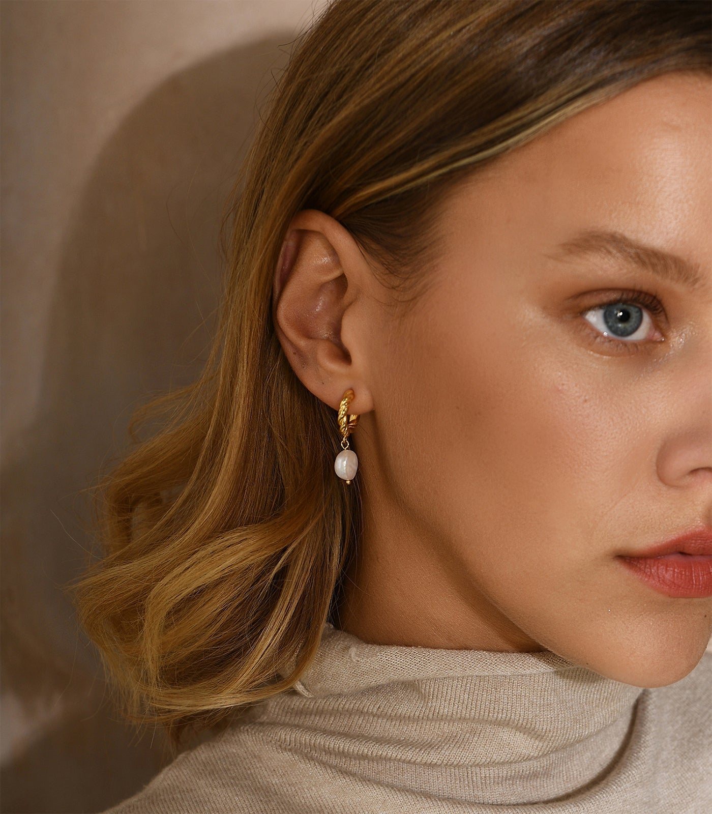 A lady wearing a twisting gold vermeil hoop with a baroque pearl hanging from the hoop.